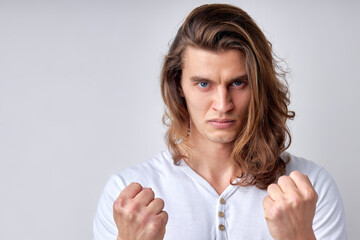 close-up portrait of angry male with long hair showing fists at camera, bad emotions. caucasian male going to fight, ready to beat, looking confident and serious. isolated light gray background