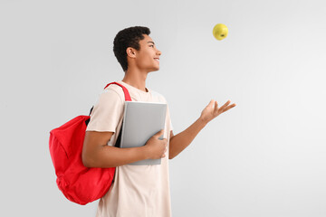 Male African-American student with notebook, backpack and apple on light background