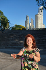 Fototapeta premium Latin mature woman smiling with her electric kick scooter, green mobility
