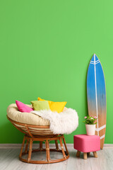 Comfortable armchair with soft pillows, pouf and surfboard near green wall in room