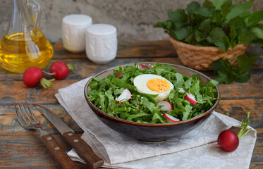 Vitamin salad from lettuce, radish, green onions and eggs, seasoned with vegetable oil in plate on wooden background. Healthy food. Salad of fresh green vegetables