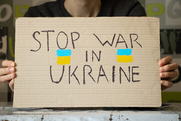 Stop the war in Ukraine written on a sign that a woman holds in her hands from her house in the...