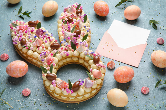 Composition with beautiful cake, painted eggs and envelope for Easter celebration on color background