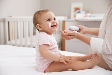 Mother applying moisturizing cream on her little baby at home, closeup