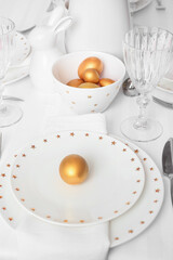 Beautiful table setting with golden Easter eggs in room, closeup