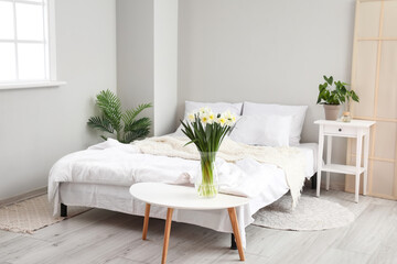 Interior of light bedroom with daffodils in vase and houseplants