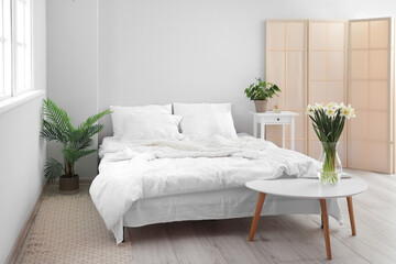 Interior of light bedroom with daffodils in vase and houseplants