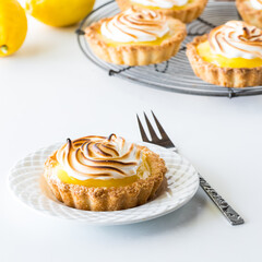 A serving of a lemon meringue tartlet and a cooling rack with more in behind.