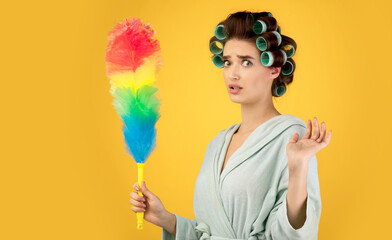 Confused Lady With Hair Curlers Holding Feather Duster, Yellow Background