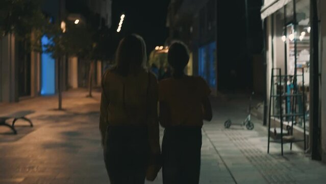 Mom and daughter walk through the night city in summer.