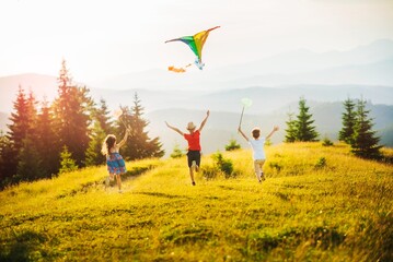 Three kids in the mountains at sunset play kite and butterfly fishing net. Happy summer holidays...