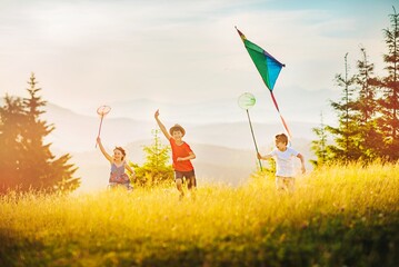 Three happy kids playing kite and butterfly net at sunset in the mountains. The concept of happy...