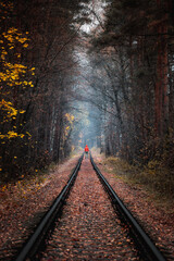Man with red coat standing on the railroad between woods.