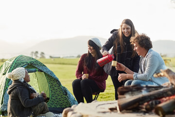 Chilled vibes only. Shot of a group of young friends enjoying coffee by the fire while on a camping...