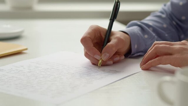A woman writes a letter on paper. Close-up.