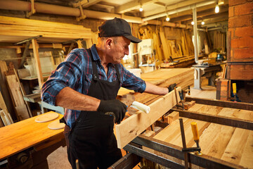 Fototapeta na wymiar Portrait of a senior carpenter in uniform gluing wooden bars with hand pressures at the carpentry manufacturing