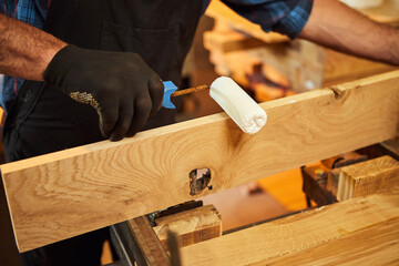 Senior carpenter in uniform gluing wooden bars with hand pressures at the carpentry