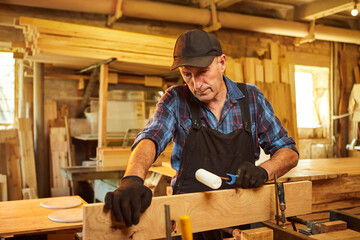 Portrait of a senior carpenter in uniform gluing wooden bars with hand pressures at the carpentry...