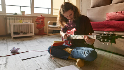 Young focused man play on electric guitar on floor
