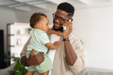 Black father talking on phone and holding baby on hands