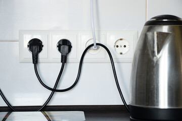 Kitchen and electric kettle on the table near the socket against the background of white tiles,...