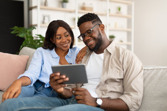 Lovely African American couple sitting on sofa, using tablet