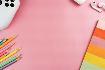 Back to school. School supplies on a pink background. Children's multi-colored accessories like crayons, notebook, scissors, video game controller. Space for text. Top view