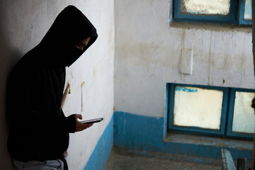 a maniac, robber, a man in a black hood is standing on the stairs, using the phone