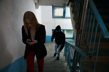 a man in a black hood is chasing a young woman on the stairs. the girl is worried, she calls the rescue service