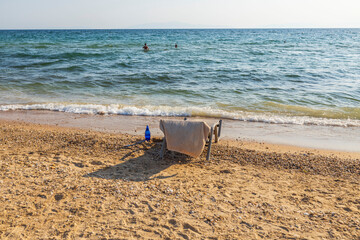 Beautiful view of sun bed on sand beach with towel and mineral bottle of water standing on on beach near water. Greece.