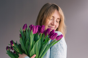 Portrait of a young woman with a bouquet of tulips on a gray background.