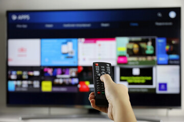 Female hand with remote controller on smart TV screen background. Woman choosing streaming...