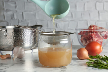 Straining delicious broth through sieve on white marble table