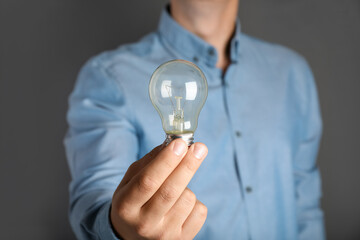 Man holding incandescent light bulb on grey background, closeup