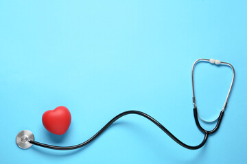 Stethoscope and red decorative heart on light blue background, flat lay with space for text. Cardiology concept