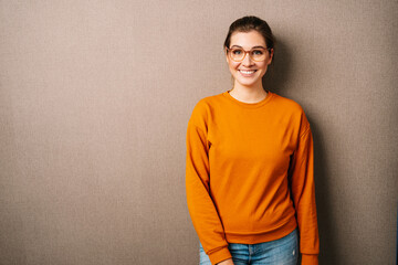 Lovely young woman grins at camera, isolated over brown background. Happiness concept