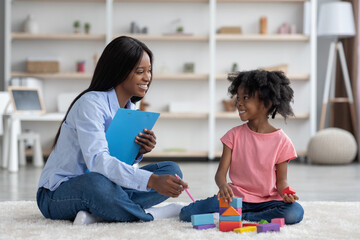 Excited african american kid and child psychotherapist playing with bricks