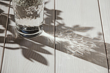 Glass of water on white table, shadows and sunlight, copy space