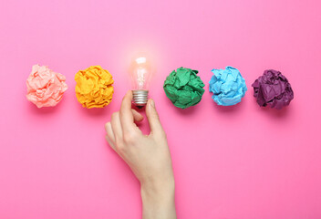 Woman holding lightbulb among colorful paper balls on pink background, top view. Idea concept