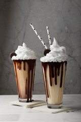 Chocolate milkshakes with whipped cream, cookies in a tall glass on a light background. Delicious dessert drink. Selective focus