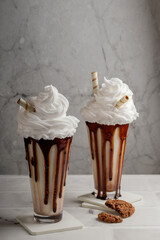 Delicious dessert. Milkshakes with chocolate with whipped cream, cookies in a tall glass on a light background. Selective focus. vertical position.