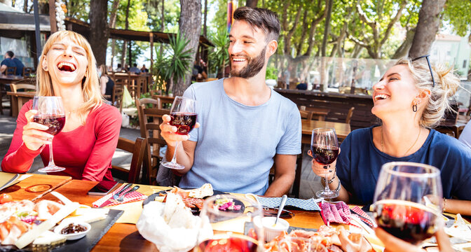 Millenial people having fun drinking red wine glasses at lunch party on sunny day - Young people eating local food at restaurant winery garden together - Dinning lifestyle concept on warm vivid filter