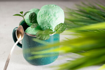 Close-up of homemade mint ice cream in a metal mug on a light background. Delicious summer dessert with fresh mint. Natural healthy food. Copy space.