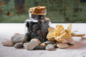 A glass bottle filled with black stones. A decorative flower on wooden sticks lies on the stones. Close-up..