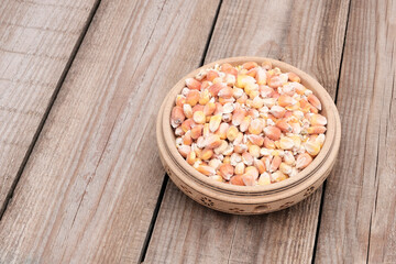 Dried corn seeds in a wooden plate on a light wood background. The concept of harvest, price increase, sanctions