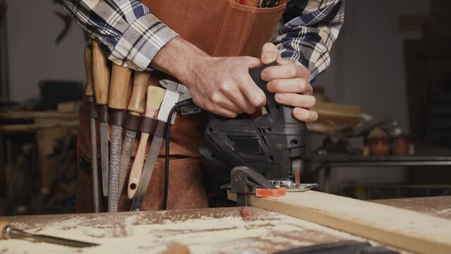 Carpenter is sawing a wood plank with electric jig saw machine in carpentry workshop. Workwood DIY concept. High quality 4k footage