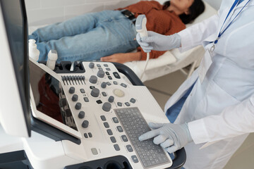 Gloved hand of female clinician pressing button on keypad of ultrasound machine while going to examine young patient on couch