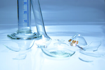 Broken laboratory glass. Measurement glass and broken flask glass on light blue background. Failed...