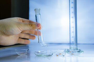 Lab measurement glass and hand holding a broken lab flask. Failed lab experiment. Chemical attempt.