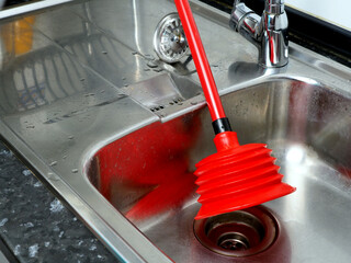 Stainless steel kitchen sink and red plunger. After clearing clogged pipes. Housework concept